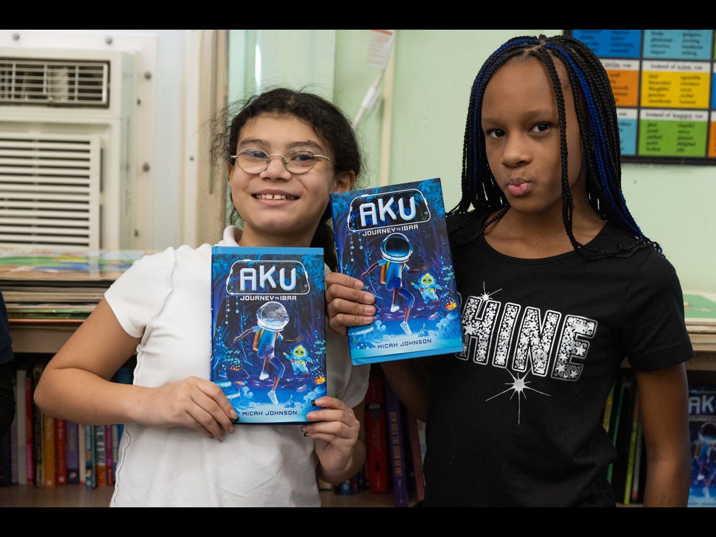 Two students holding copies of Aku: Journey to Ibra in their classroom.